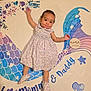 Maxyne is registered to the contest to win money with this photo: baby, infant, dress, booties, blanket, mermaid, milestone_marker, carpet, floor, child, cute, smiling, lying_down, patterned_clothing, indoor, toy, colorful, purple, blue, decorative