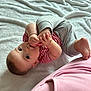 baby, infant, child, blanket, striped_clothing, gray_pants, sucking_thumb, foot, lying_down, curious, soft_texture, indoor, cute, playful, skin, head, eyes, hand, person, cozy