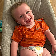 Luca joined the competition — help win amazing prizes! baby, smiling, orange_shirt, diaper, cushion, seat, child, happy, indoor, floor, wooden_floor, toy, infant, cute, person, portrait, skin, face, clothing, relaxing