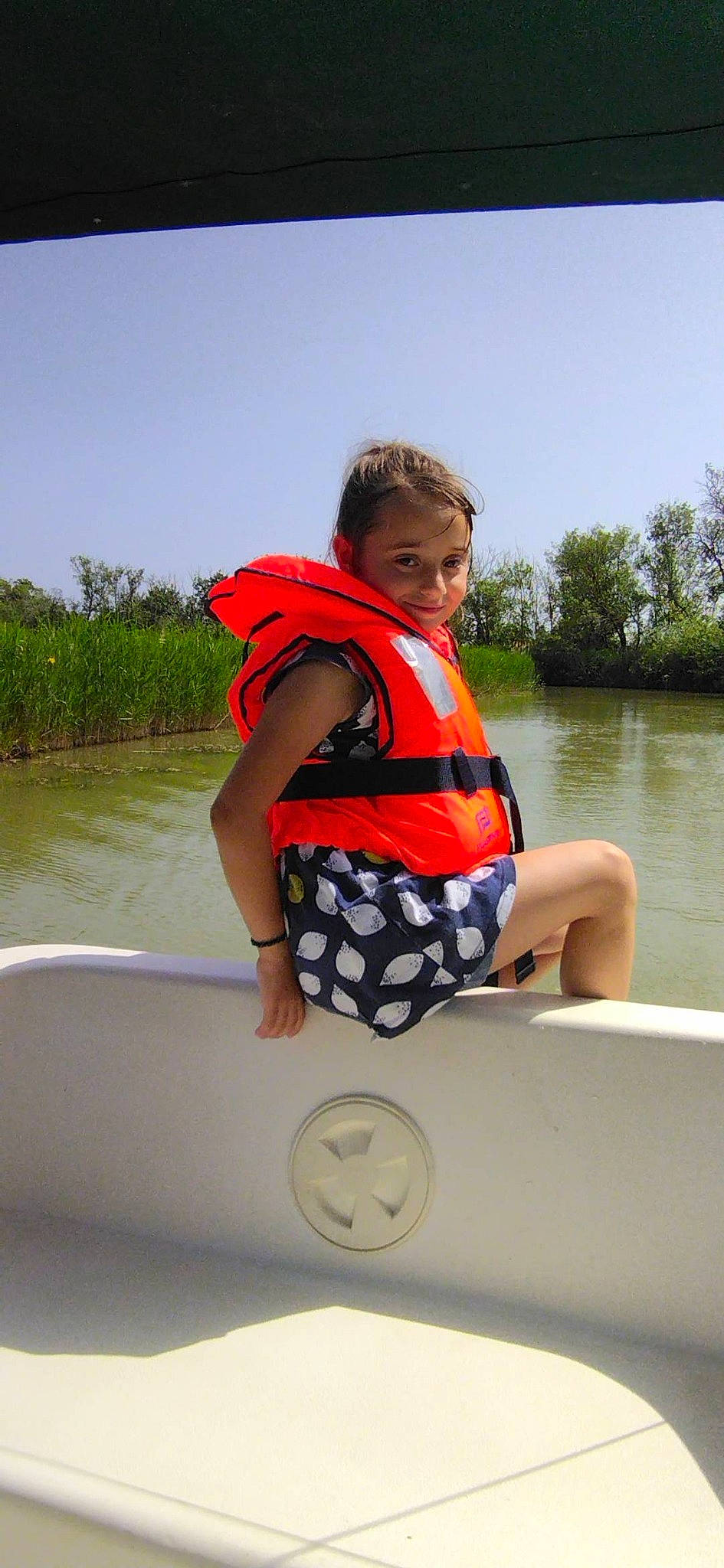 Anna participe au concours pour gagner de l'argent avec cette photo : boat, boats_and_boating_equipment_and_supplies, fun, joy, lake, leisure, lifejacket, person, personal_protective_equipment, plant, recreation, sitting, sky, sports, toddler, travel, tree, vehicle, vest, water