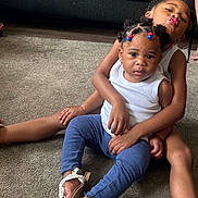 Armani is registered to the contest to win money with this photo: child, children, baby, carpet, indoor, couch, braided_hair, beads, white_shirt, blue_pants, sandals, smiling, playful, sitting, family, cute, portrait, toddler, candid, affection