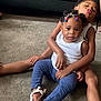 child, children, baby, carpet, indoor, couch, braided_hair, beads, white_shirt, blue_pants, sandals, smiling, playful, sitting, family, cute, portrait, toddler, candid, affection