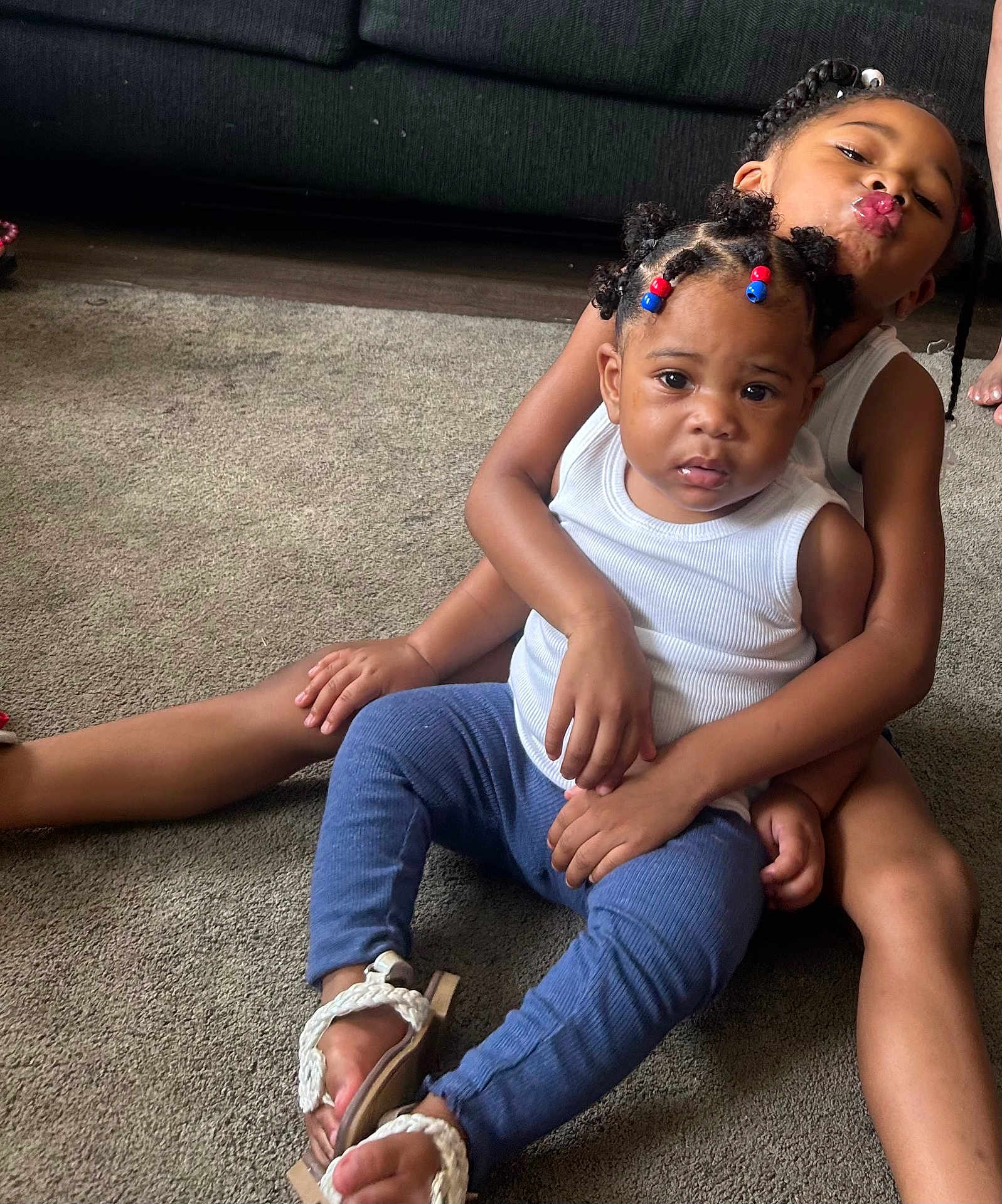 Armani is registered to the contest to win money with this photo: child, children, baby, carpet, indoor, couch, braided_hair, beads, white_shirt, blue_pants, sandals, smiling, playful, sitting, family, cute, portrait, toddler, candid, affection