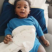 Jaheim a rejoint le concours — aidez-le/la à gagner de superbes lots ! baby, child, blue_clothing, blanket, couch, pillow, indoor, infant, relaxing, smiling, young_child, person, face, hand, cozy, home, soft_fabric, comfort, curious, portrait