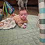 baby, infant, play_mat, plush_toy, elephant_toy, hanging_toys, floor, wooden_floor, quilted_mat, clothing, person, indoor, cute, child, curious, small_hands, face, head, baby_girl, soft_toys