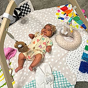 Jimena joined the competition — help win amazing prizes! baby, infant, play_mat, toy, wooden_toy, headband, romper, colorful, soft_toy, floor, carpet, child, cute, smiling, lying_down, indoor, playtime, fabric, patterned, happy