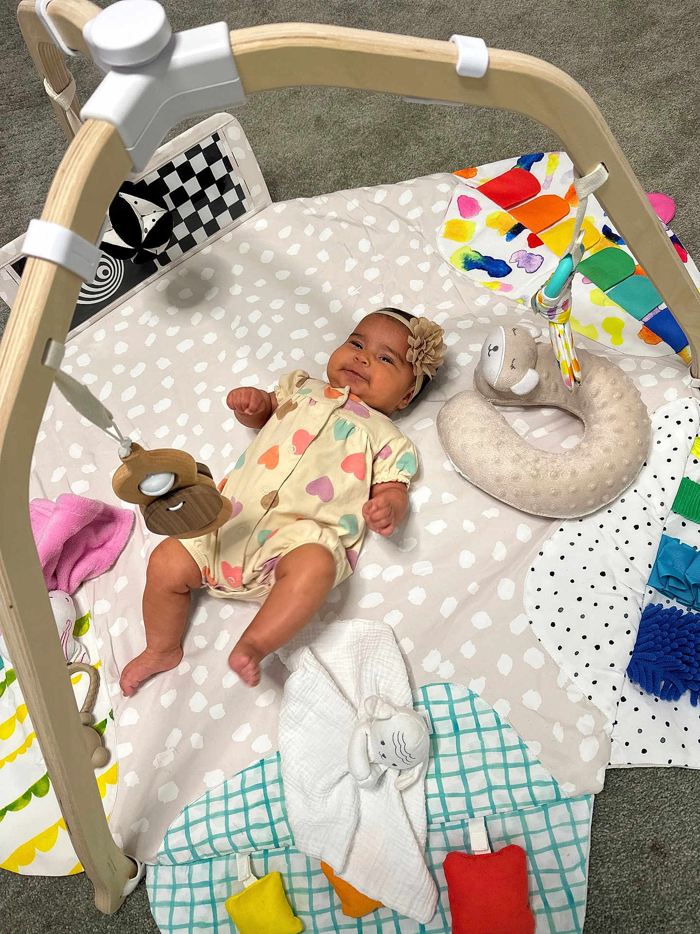 Jimena joined the competition — help win amazing prizes! baby, infant, play_mat, toy, wooden_toy, headband, romper, colorful, soft_toy, floor, carpet, child, cute, smiling, lying_down, indoor, playtime, fabric, patterned, happy