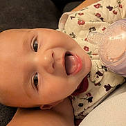 Addison joined the competition — help win amazing prizes! baby, infant, face, smiling, bottle, feeding, child, cute, closeup, floral_clothing, tongue, lying_down, happy, skin, head, eyes, mouth, person, newborn, cozy