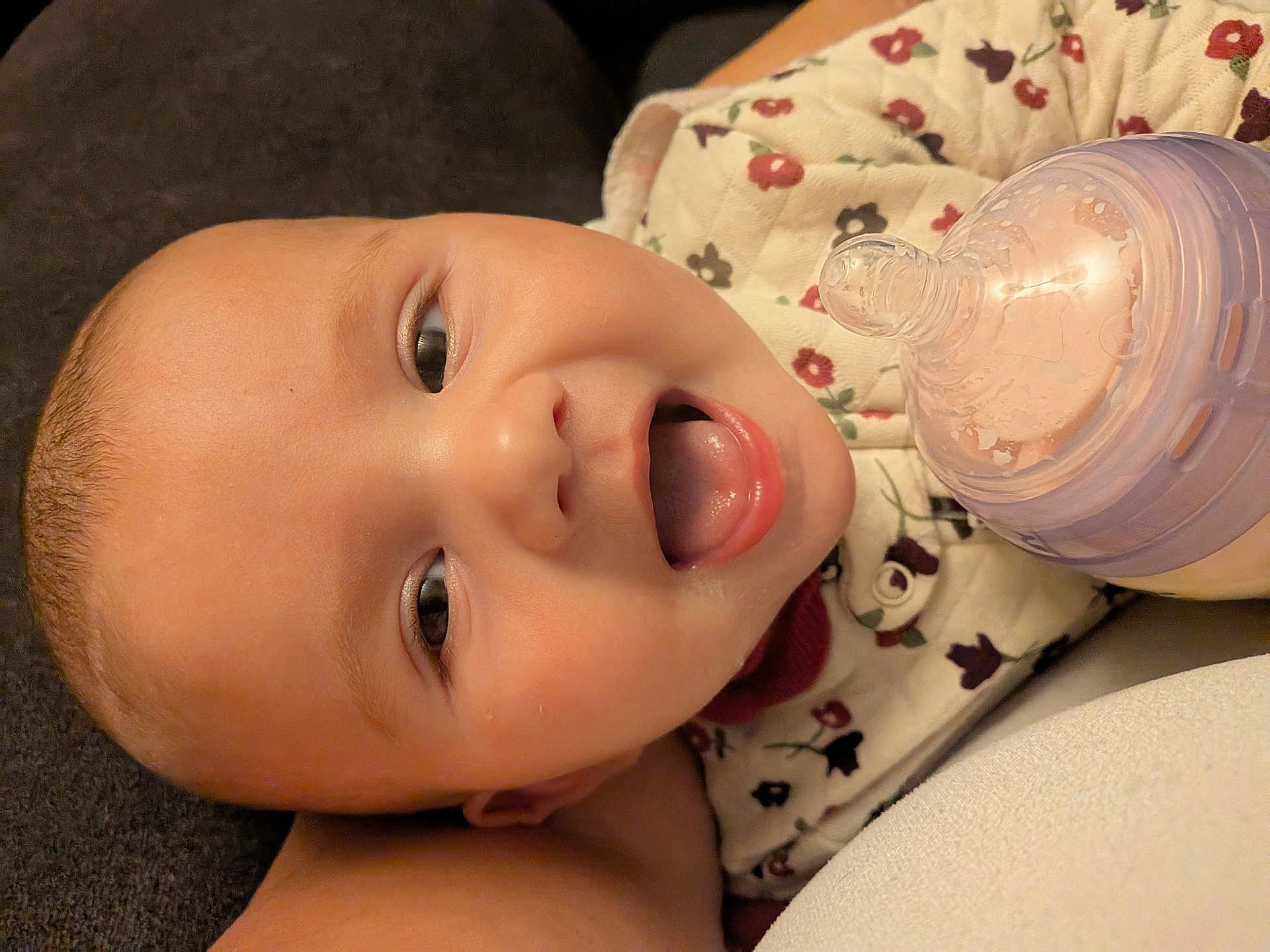 Addison joined the competition — help win amazing prizes! baby, infant, face, smiling, bottle, feeding, child, cute, closeup, floral_clothing, tongue, lying_down, happy, skin, head, eyes, mouth, person, newborn, cozy