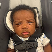 Yanis is registered to the contest to win money with this photo: baby, infant, car_seat, seatbelt, straps, clothing, expression, face, human, child, portrait, indoor, cute, serious, closeup, person, newborn, sitting, padded, safety