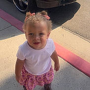 Eternity joined the competition — help win amazing prizes! toddler, child, girl, sidewalk, curly_hair, pigtails, pink_ribbons, white_tshirt, floral_skirt, cowboy_boots, car_wheel, parked_car, outdoor, sunlight, concrete, curious_expression, standing, urban, daytime, shadow