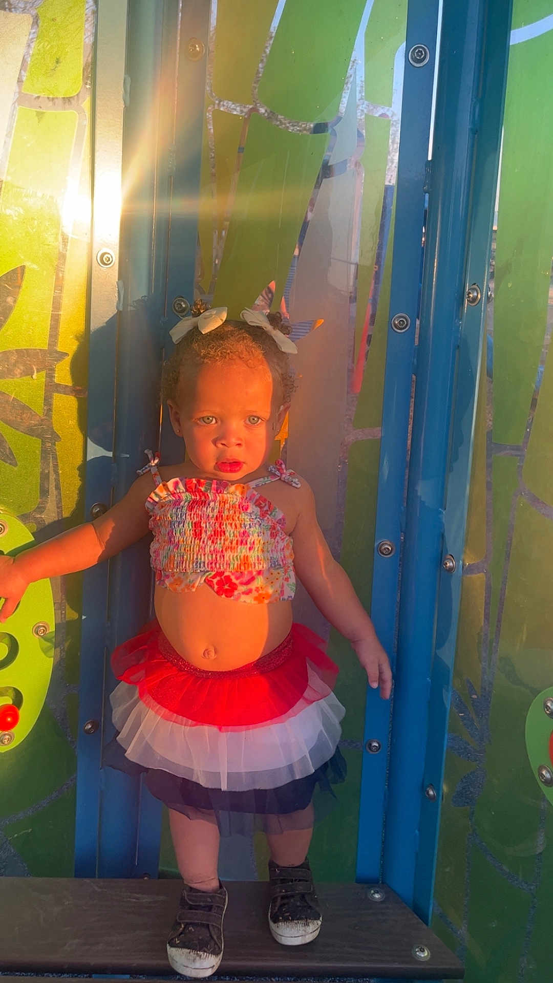 Eternity is registered to the contest to win money with this photo: toddler, child, playground, sunlight, lens_flare, colorful_clothing, hair_buns, bows, skirt, shoes, platform, metal_structure, outdoor, summer, cute, standing, expression, person, young_child, daylight