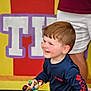 Tate is registered to the contest to win money with this photo: child, boy, toy, smiling, playing, indoor, person, short_hair, blue_shirt, columbia_branded, hand, adult_support, background, colorful_wall, wooden_floor, figure, vehicle_toy, happy, casual_clothing, portrait