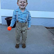 Tate is registered to the contest to win money with this photo: toddler, child, boy, smiling, suspenders, blue_shirt, beige_pants, brown_shoes, basketball, outdoor, concrete_floor, wall, standing, happy, short_hair, casual_clothing, playing, daylight, portrait, cute