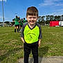 Tate is registered to the contest to win money with this photo: child, boy, soccer, sports, field, grass, outdoor, daylight, team, jersey, smile, happy, green, black, shoes, people, sky, trees, casual, portrait