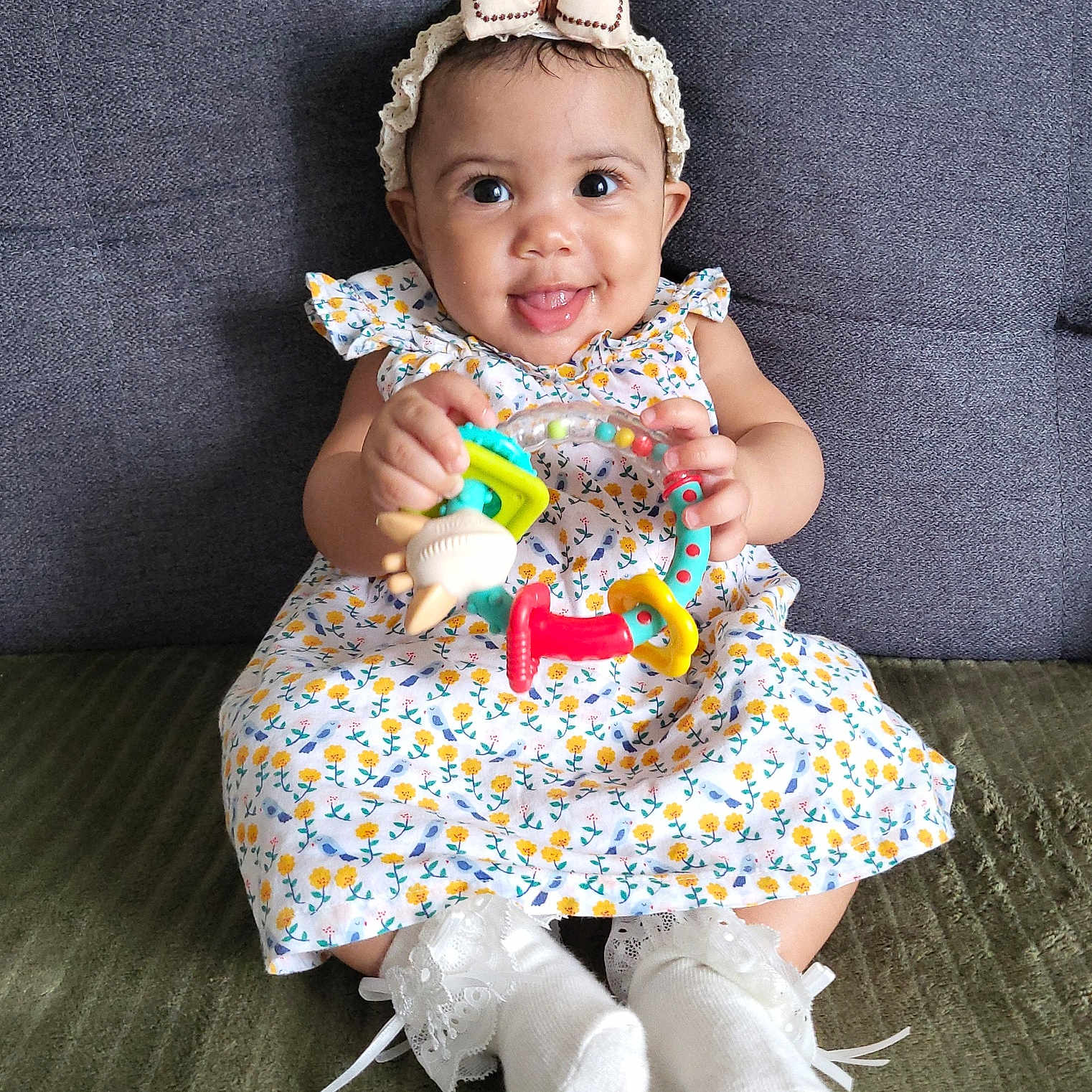 Youvina a rejoint le concours — aidez-le/la à gagner de superbes lots ! baby, bow, child, colorful_toy, couch, cute, dress, floral_pattern, happy, headband, indoor, infant, lace, person, playful, portrait, seated, smiling, socks, toy