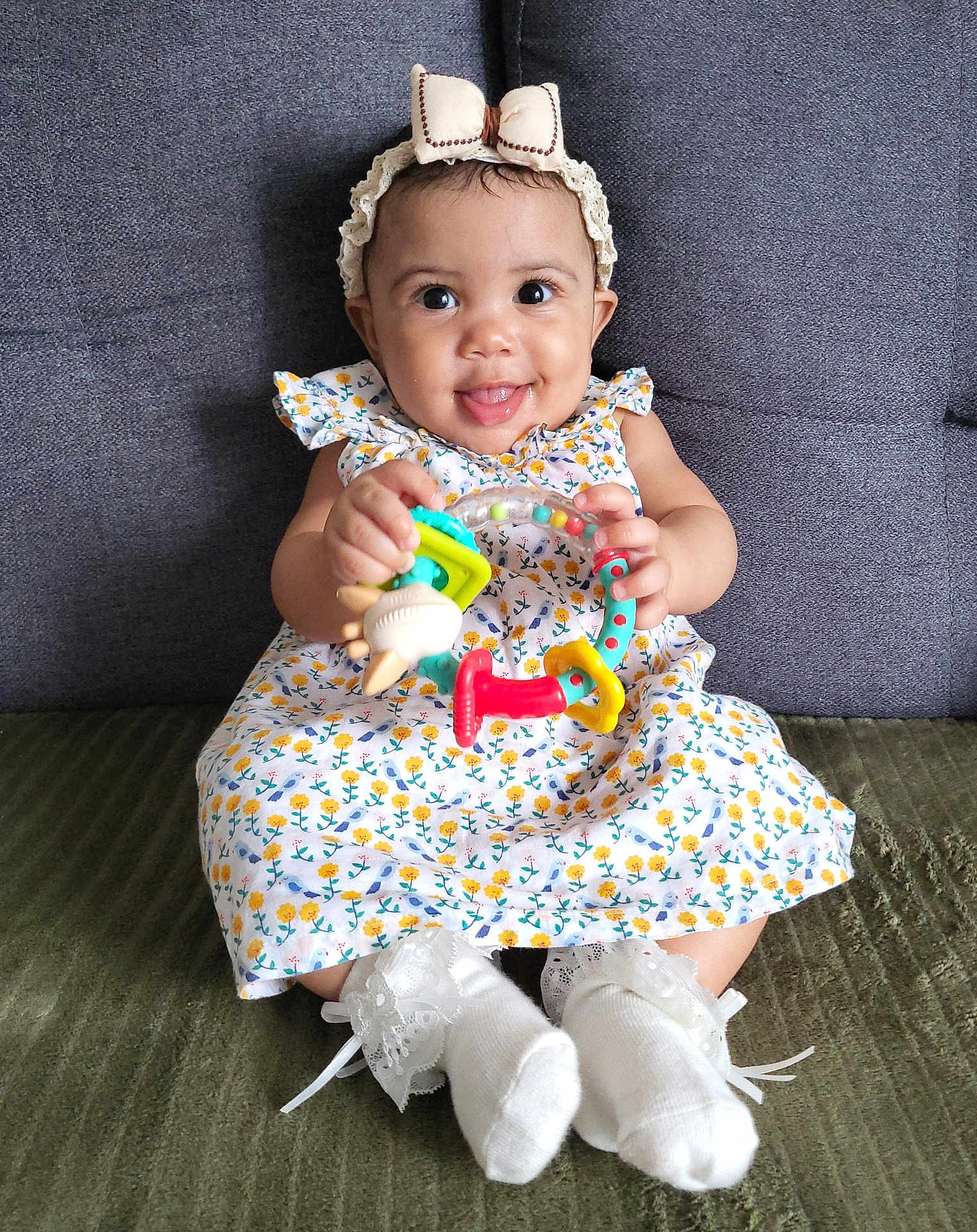 Youvina a rejoint le concours — aidez-le/la à gagner de superbes lots ! baby, child, smiling, toy, colorful_toy, dress, floral_pattern, headband, bow, socks, lace, couch, seated, happy, indoor, person, cute, playful, infant, portrait
