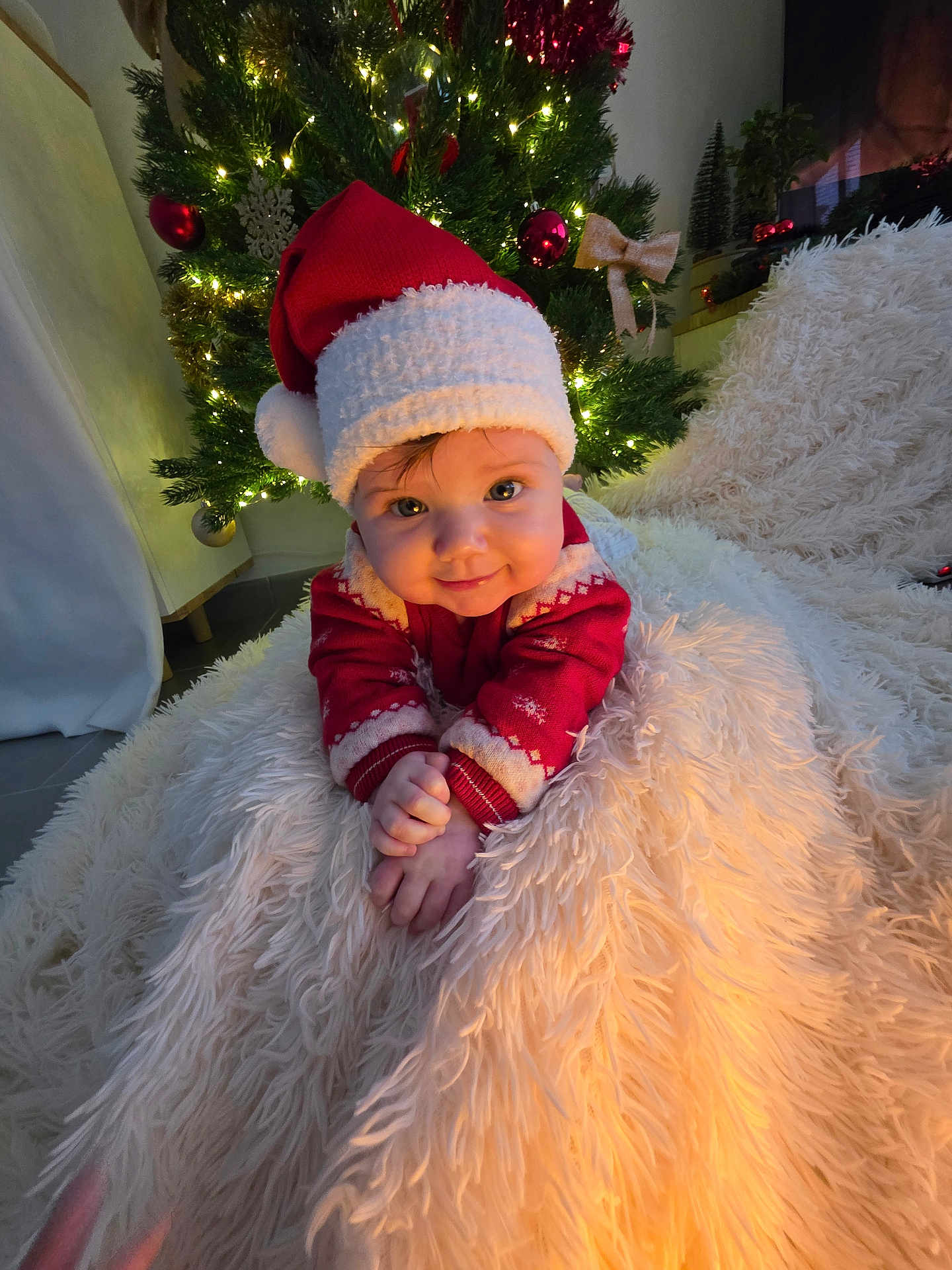 Hanna participe au concours pour gagner de l'argent avec cette photo : baby, christmas_hat, christmas_tree, holiday, festive, smiling, cute, red_clothing, white_blanket, indoor, decorations, lights, ornaments, cozy, child, portrait, seasonal, celebration, happy, holiday_spirit