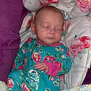 Luna is registered to the contest to win money with this photo: baby, sleeping, infant, onesie, floral_pattern, blanket, cushion, purple, face, hand, cozy, resting, newborn, child, comfort, portrait, indoors, cute, peaceful, soft