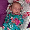 baby, sleeping, infant, onesie, floral_pattern, blanket, cushion, purple, face, hand, cozy, resting, newborn, child, comfort, portrait, indoors, cute, peaceful, soft