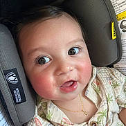 Evan is registered to the contest to win money with this photo: baby, child, face, car_seat, seat_belt, clothing, necklace, patterned_shirt, rosy_cheeks, happy, curious, indoor, close_up, infant, cute, person, young_child, eyelashes, buttoned_shirt, head_support
