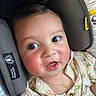 baby, child, face, car_seat, seat_belt, clothing, necklace, patterned_shirt, rosy_cheeks, happy, curious, indoor, close_up, infant, cute, person, young_child, eyelashes, buttoned_shirt, head_support