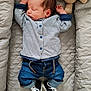 baby, newborn, sleeping, striped_shirt, denim_pants, sneakers, quilted_cushion, crocheted_toy, teddy_bear, infant, cozy, indoor, cute, child, soft_lighting, peaceful, portrait, clothing, resting, small_hands