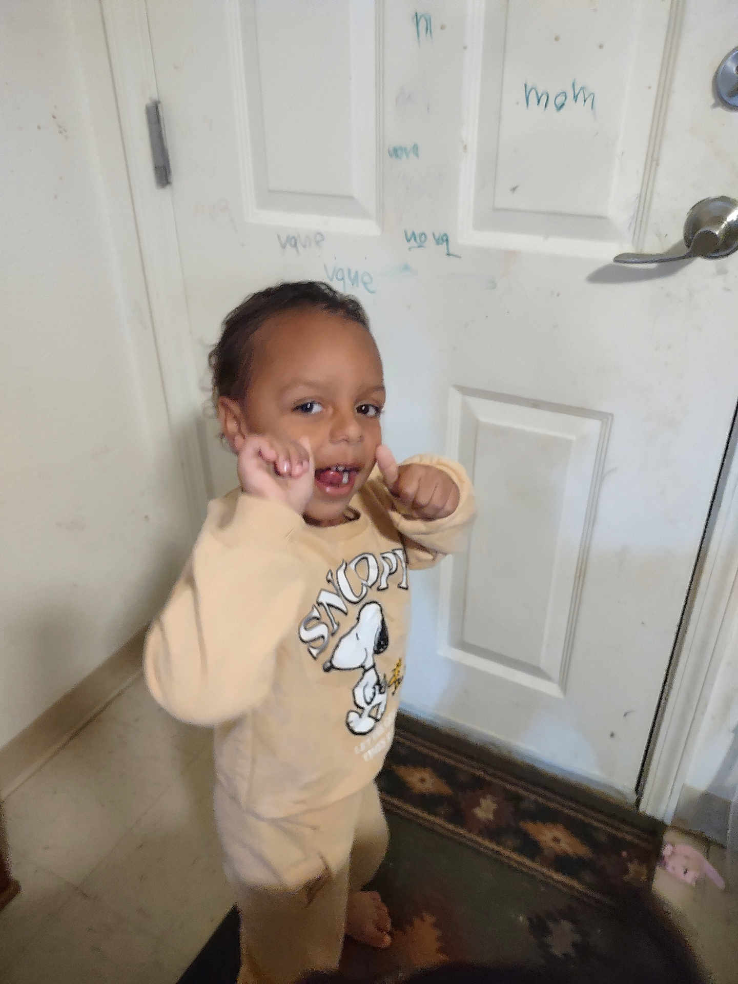 Koda is registered to the contest to win money with this photo: child, toddler, sweatshirt, snoopy, smile, thumbs_up, indoors, door, scribbles, rug, barefoot, person, clothing, floor, carpet, hand_gesture, cute, expression, young_child, wall