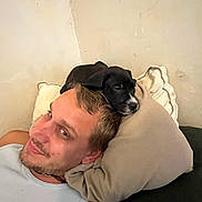 Speak participe au concours pour gagner de l'argent avec cette photo : man, puppy, dog, couch, pillow, relaxing, indoor, smile, face, laying_down, casual, pet, cute, comfort, head, furniture, resting, young_adult, black_dog, home