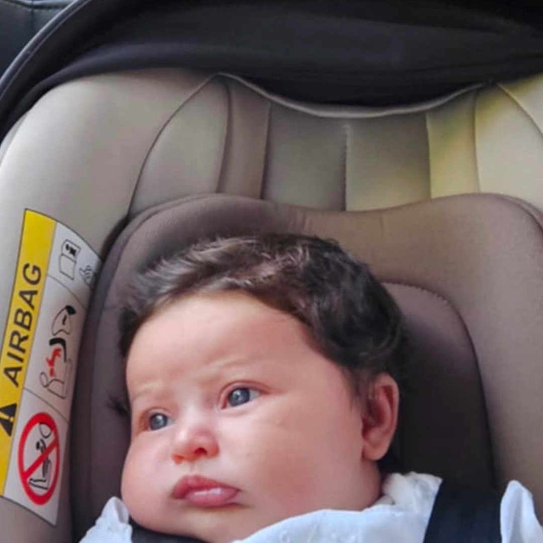 Esmeray-Rose is registered to the contest to win money with this photo: baby, blue_eyes, buckle, car_interior, car_seat, child, chubby_cheeks, curly_hair, cute, face, head_support, indoors, infant, person, portrait, safety_strap, seat_belt, sitting, white_clothing, young_child