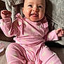 baby, infant, smiling, pink_clothing, heart_pattern, tongue_out, cute, happy, portrait, sitting, blanket, soft_texture, indoors, child, person, baby_clothes, cute_expression, closeup, warm, cozy
