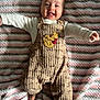 Milani is registered to the contest to win money with this photo: baby, smiling, infant, overalls, winnie_the_pooh, blanket, striped, cozy, cute, happy, tongue, person, child, soft_texture, lying_down, clothing, indoor, portrait, face, apparel