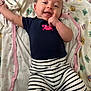 Milani is registered to the contest to win money with this photo: baby, infant, smiling, lying_down, striped_pants, navy_shirt, pink_crab, blanket, colorful_pattern, happy, cute, child, one_person, indoors, young_child, playful, casual_clothing, skin, face, hand