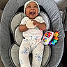baby, infant, child, smiling, laughing, portrait, sitting, baby_seat, cushion, hat, onesie, clothing, toy, rattle, caterpillar_toy, colorful, indoors, happy, playful, photography