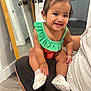 toddler, child, smiling, indoor, mirror, green_clothing, orange_clothing, white_shoes, sitting, person, flooring, door, reflection, hair_tie, cute, happy, baby, hand, face, portrait