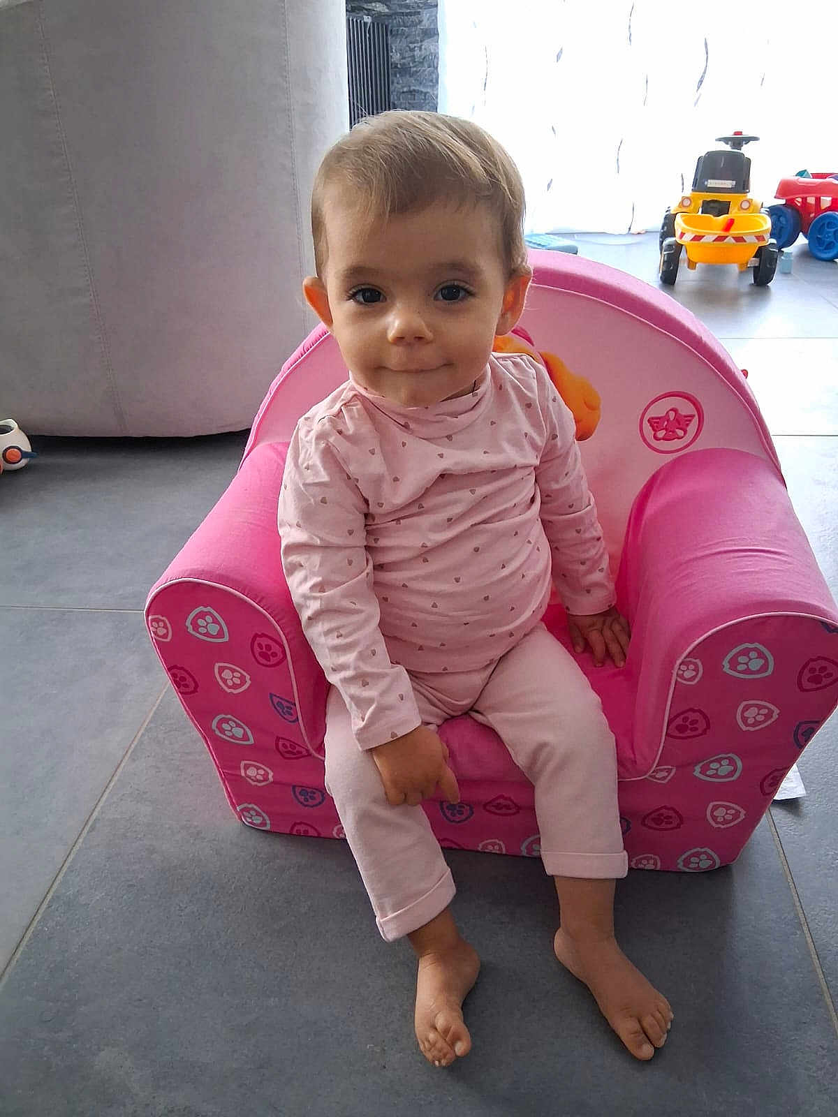 Victoria a rejoint le concours — aidez-le/la à gagner de superbes lots ! toddler, child, pink_chair, pajamas, indoor, toys, floor, curious, sitting, barefoot, home, relaxed, young_child, furniture, person, casual_clothing, portrait, cute, baby, playroom