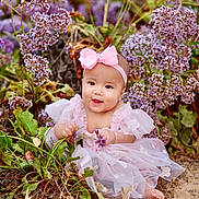 Mika is registered to the contest to win money with this photo: baby, infant, child, pink_dress, headband, bow, flowers, purple_flowers, outdoor, nature, plants, greenery, cute, smiling, sitting, ground, portrait, garden, floral, happy