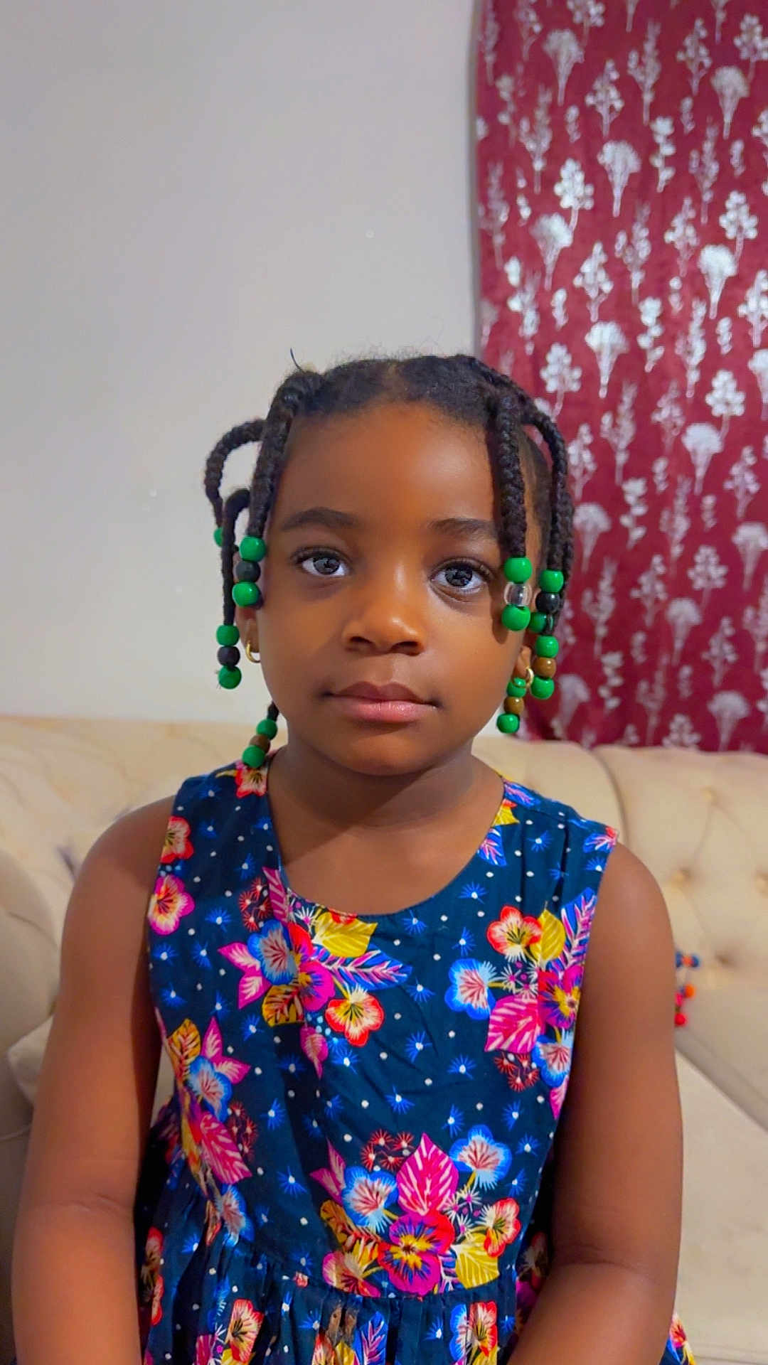 Lea participe au concours pour gagner de l'argent avec cette photo : child, girl, braids, beads, dress, floral_pattern, couch, indoor, portrait, face, calm, seated, furniture, curtain, pattern, colorful, person, young, hairstyle, casual