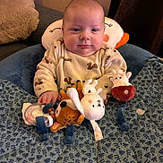 Lysio participe au concours pour gagner de l'argent avec cette photo : baby, infant, plush_toy, stuffed_animal, blanket, pillow, sitting, indoors, child, clothing, cute, face, person, soft_toy, comfort, patterned_blanket, head_support, happy, smile, cozy