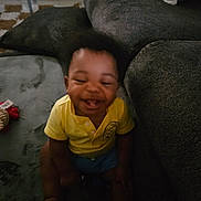 Micah joined the competition — help win amazing prizes! toddler, child, smiling, yellow_shirt, carpet, couch, indoor, happy, sitting, blurred, joyful, young_child, living_room, furniture, person, home, cozy, candid, afro_hair, playful
