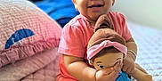 Zoe joined the competition — help win amazing prizes! baby, bed, bracelet, child, curly_hair, cute, doll, happy, home, indoors, person, pink_clothing, playful, portrait, quilt, seated, smiling, socks, soft_light, toy