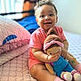 baby, bed, bracelet, child, curly_hair, cute, doll, happy, home, indoors, person, pink_clothing, playful, portrait, quilt, seated, smiling, socks, soft_light, toy