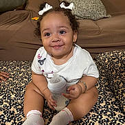 Zoe joined the competition — help win amazing prizes! baby, blanket, bottle, bracelet, child, couch, curly_hair, cute, floral_pattern, hair_bows, happy, indoor, infant, milk, person, pillow, sitting, smiling, socks, white_shirt