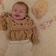 Alyana participe au concours pour gagner de l'argent avec cette photo : baby, infant, smile, lying_down, soft_toy, plush, beige_clothing, white_pants, fluffy_rug, cute, young_child, face, happy, cozy, portrait, indoor, child, wearing_clothes, decor, small