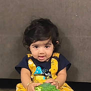 Sitara is registered to the contest to win money with this photo: toddler, child, broccoli, yellow_clothing, curly_hair, indoor, cute, holding, food, playful, portrait, person, sitting, expression, young_child, casual, baby, face, eyes, hands