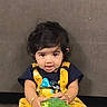 toddler, child, broccoli, yellow_clothing, curly_hair, indoor, cute, holding, food, playful, portrait, person, sitting, expression, young_child, casual, baby, face, eyes, hands