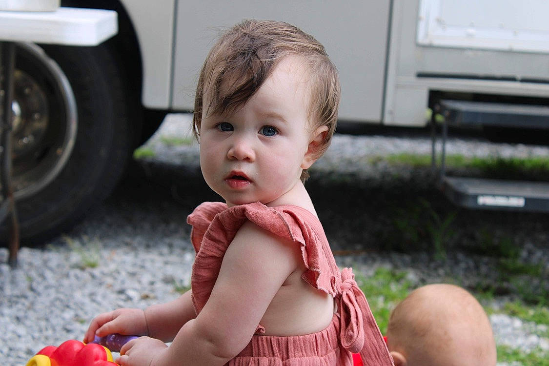 Athena is registered to the contest to win money with this photo: asphalt, automotive_tire, baby, baby_toddler_clothing, child, dress, facial_expression, fun, grass, hand, happy, leisure, orange, people, person, red, summer, tire, toddler, wheel