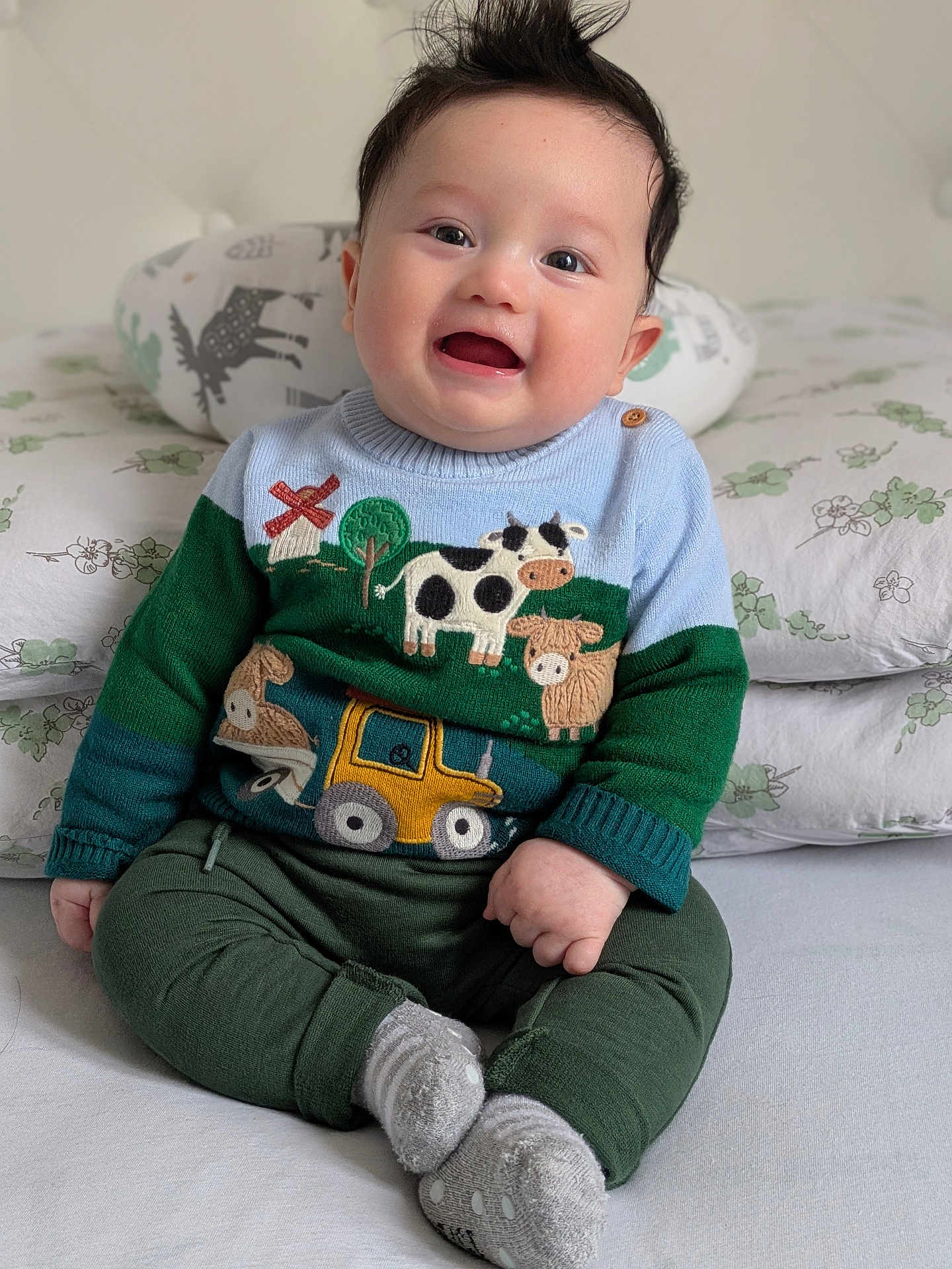 Théo participe au concours pour gagner de l'argent avec cette photo : baby, child, smiling, sitting, sweater, clothing, face, pillow, bed, indoors, cute, happy, person, portrait, green_pants, gray_socks, hair, toy_motif, fabric, cozy