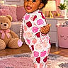 child, toddler, baby, portrait, smiling, standing, indoor, nursery, pajamas, curly_hair, dark_skin, teddy_bear, pacifier, pink, colorful, playroom, rug, lamp, window, furniture