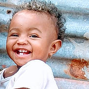 Maïssane participe au concours pour gagner de l'argent avec cette photo : toddler, child, smiling, happy, face, curly_hair, earring, white_shirt, portrait, closeup, skin, teeth, rusty_background, metal, outdoor, candid, cute, person, joy, expression